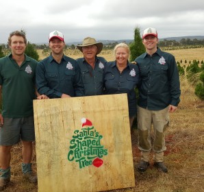 The Santa's Shaped Christmas Tree Farm family holding the farm sign among the tree rows